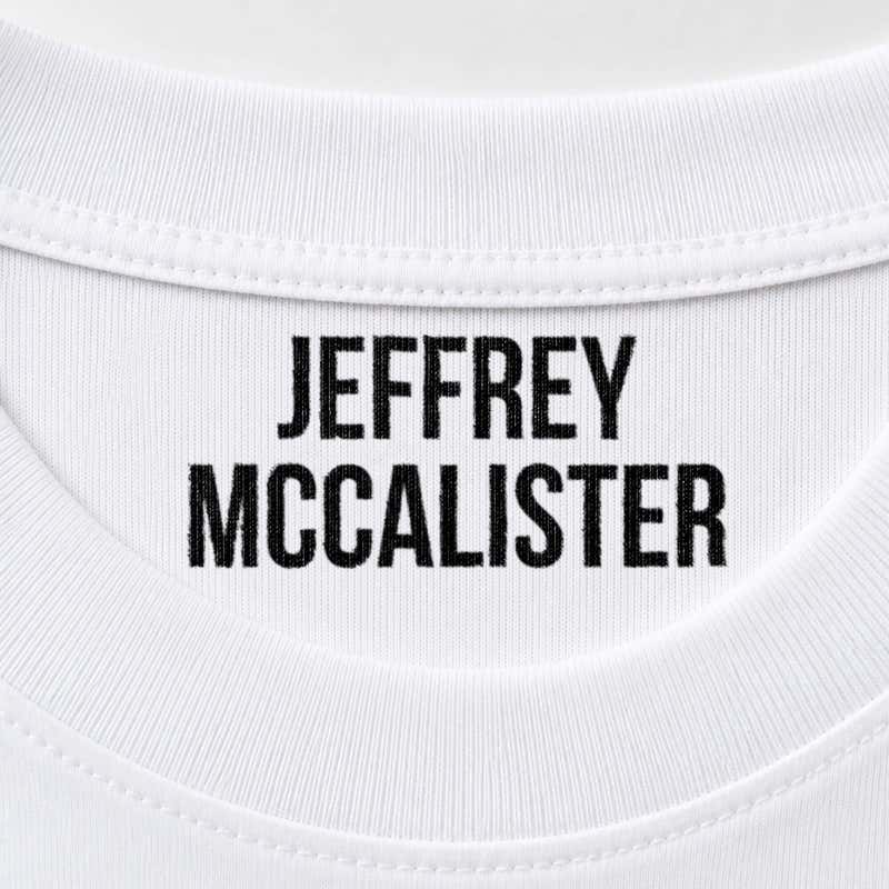 Close-up of a name stamped inside a white t-shirt collar in the Bold font, a heavy condensed all-caps print.