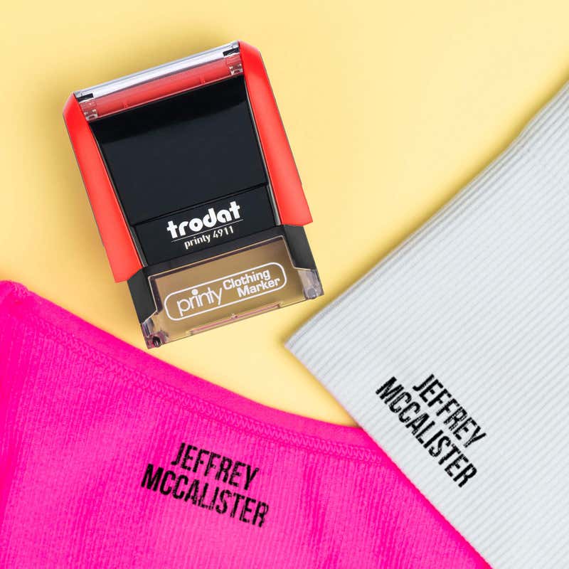 A pink shirt and a gray sock name-stamped in the Bold font, a heavy condensed all-caps print, beside a Trodat clothing stamp, on a yellow background.