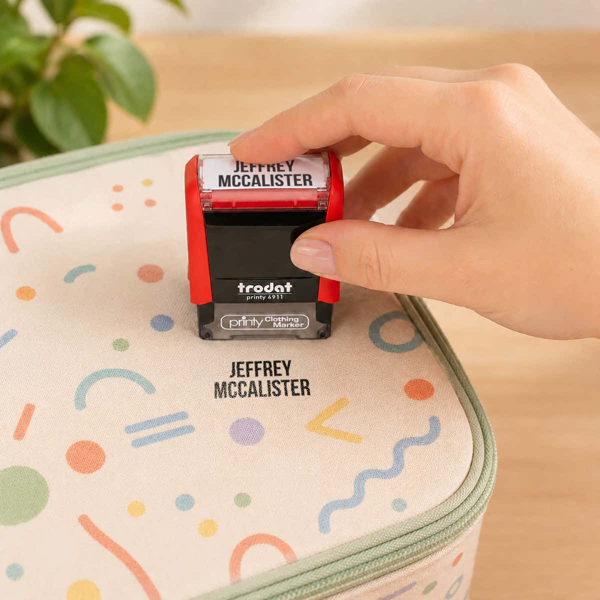 Hand stamping a patterned lunch bag with a name in the Bold font, a heavy condensed all-caps print, using a Trodat clothing stamp.