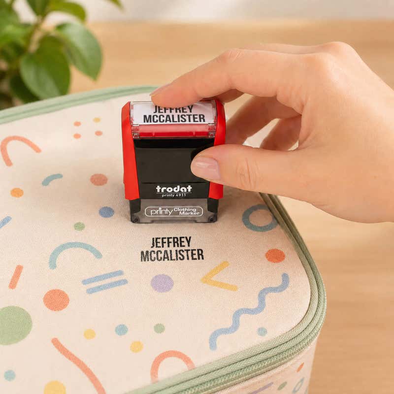 Hand stamping a patterned lunch bag with a name in the Bold font, a heavy condensed all-caps print, using a Trodat clothing stamp.