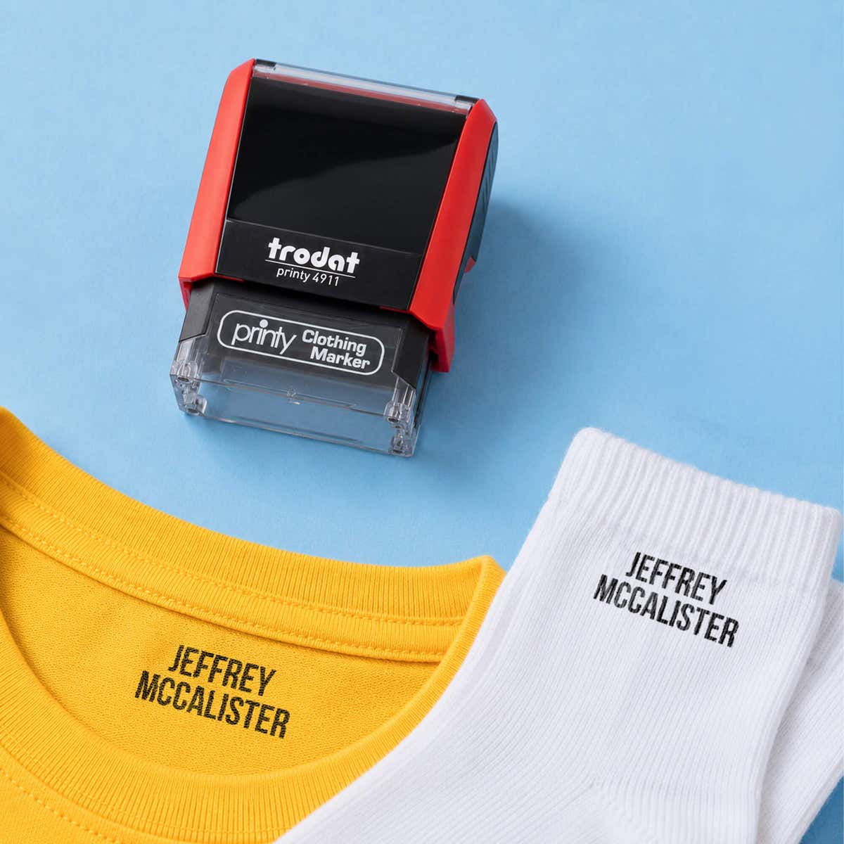 A t-shirt collar and sock name-stamped in the Bold font, a heavy condensed all-caps print, beside a Trodat clothing stamp, on a blue background.