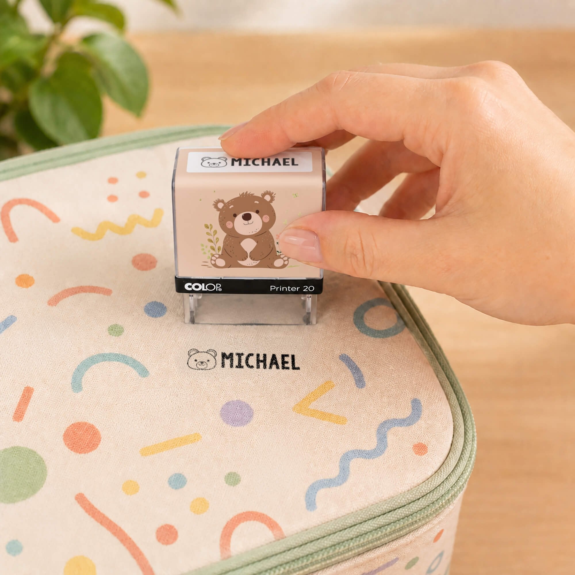Hand using a bear clothing name stamp to label a patterned lunch bag Michael
