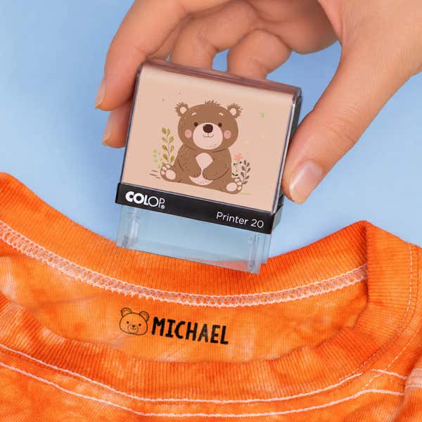 Hand holding a bear clothing name stamp above an orange shirt labeled Michael