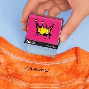 Hand holding a crown clothing name stamp above an orange shirt labeled Harrison