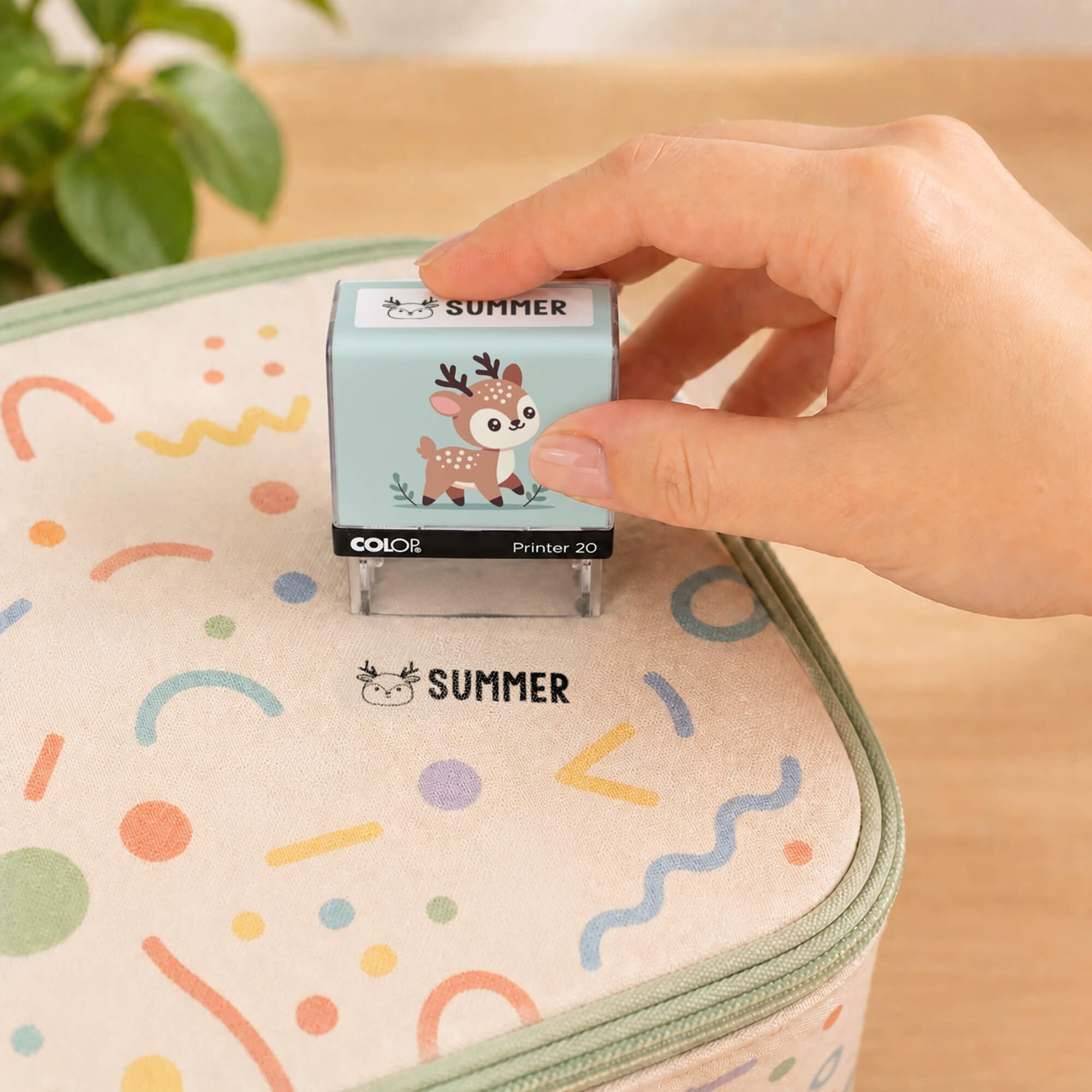 Hand using a deer clothing name stamp to label a patterned lunch bag Summer