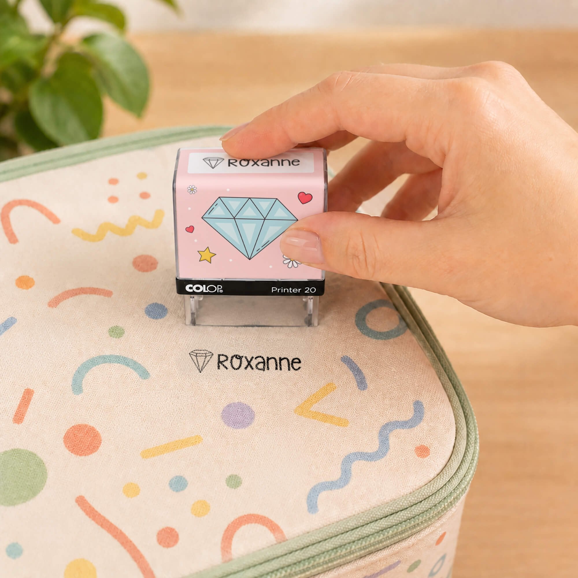 Hand using a diamond clothing name stamp to label a patterned lunch bag Roxanne
