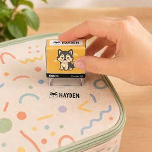 Hand using a dog clothing name stamp to label a patterned lunch bag Hayden