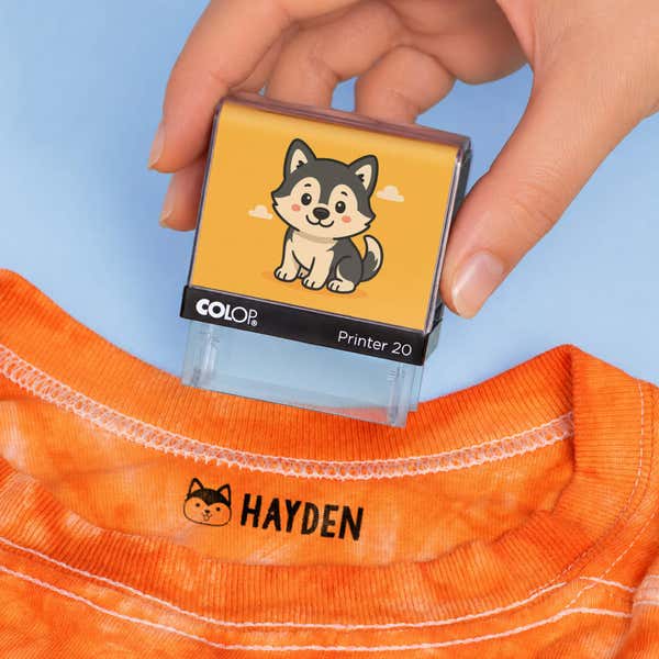 Hand holding a dog clothing name stamp above an orange shirt labeled Hayden