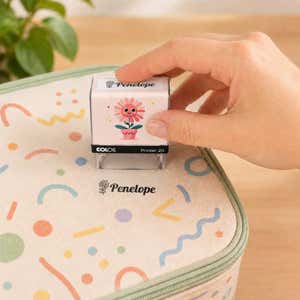 Hand using a flower clothing name stamp to label a patterned lunch bag Penelope