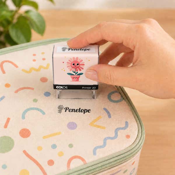 Hand using a flower clothing name stamp to label a patterned lunch bag Penelope