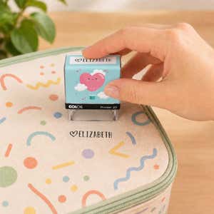 Hand using a heart clothing name stamp to label a patterned lunch bag Elizabeth