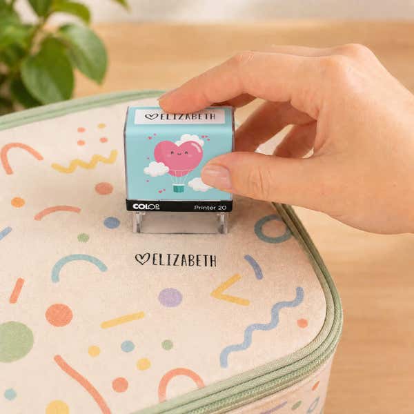 Hand using a heart clothing name stamp to label a patterned lunch bag Elizabeth