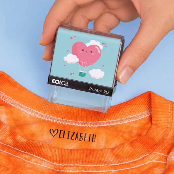 Hand holding a heart clothing name stamp above an orange shirt labeled Elizabeth