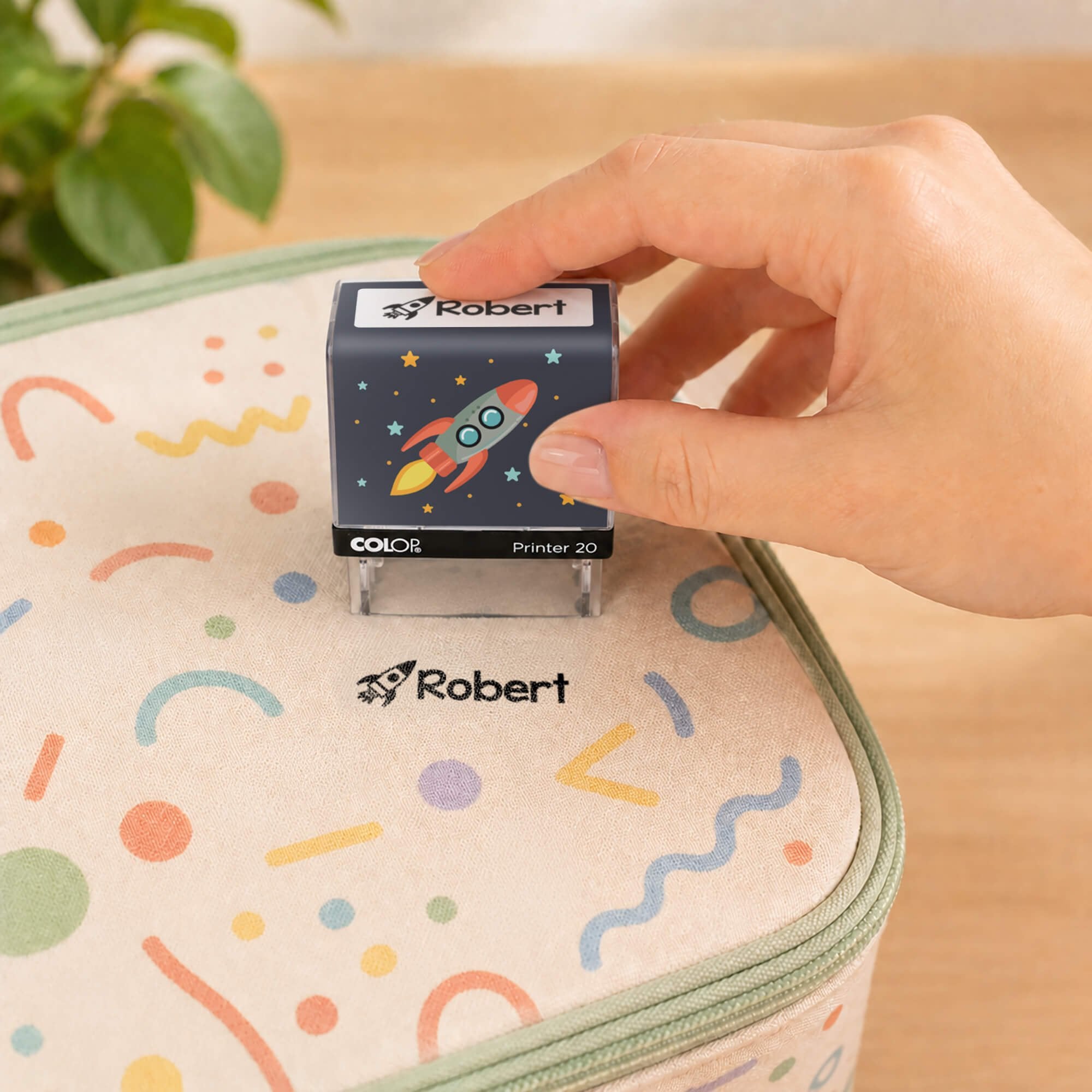 Hand using a rocket clothing name stamp to label a patterned lunch bag Robert