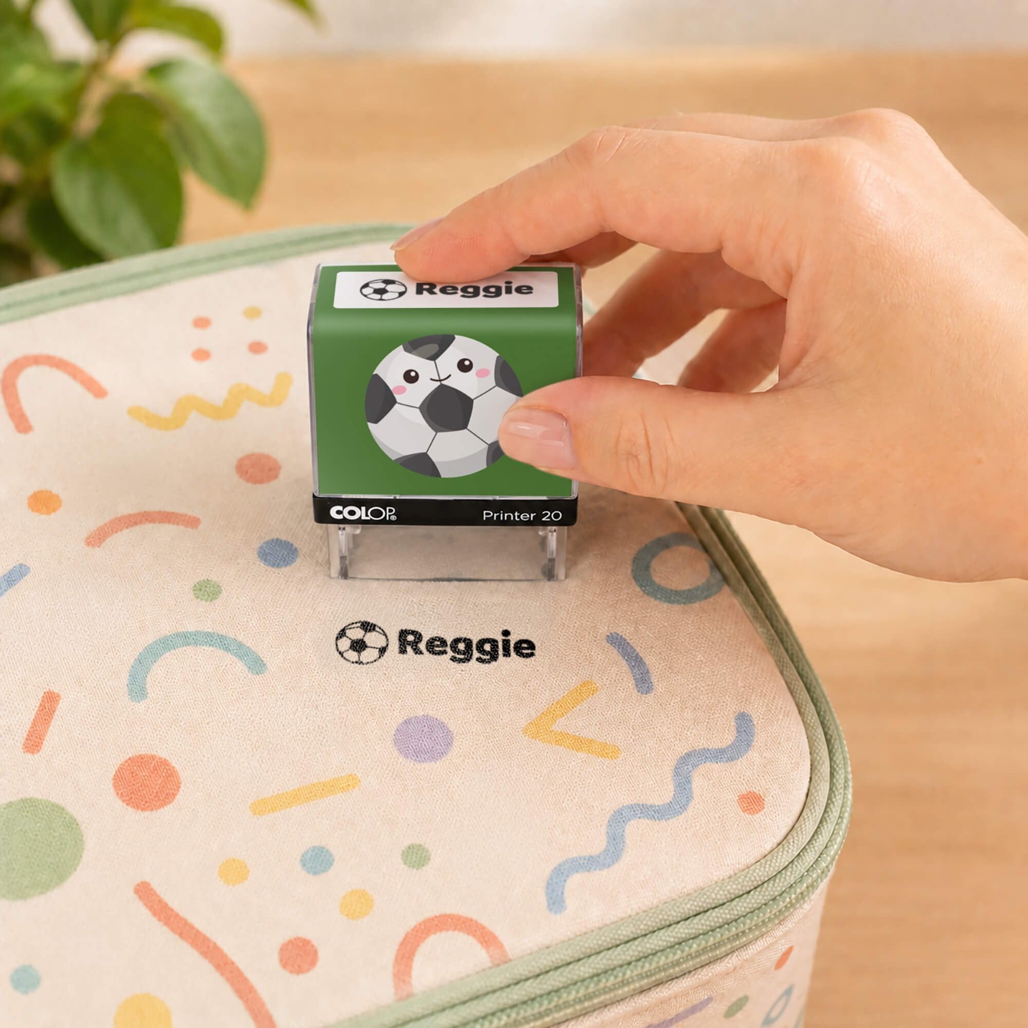 Hand using a soccer clothing name stamp to label a patterned lunch bag Reggie