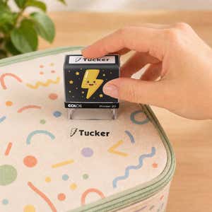 Hand using a thunder bolt clothing name stamp to label a patterned lunch bag Tucker