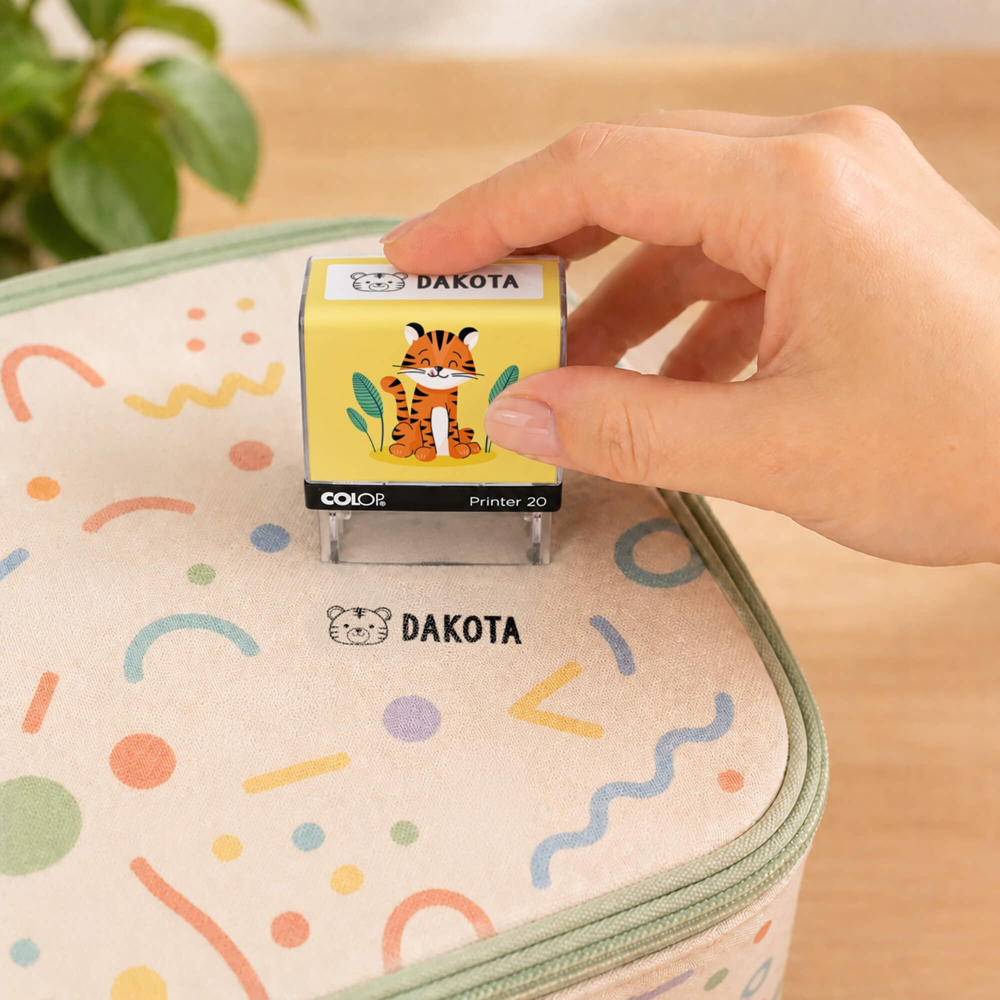 Hand using a tiger clothing name stamp to label a patterned lunch bag Dakota