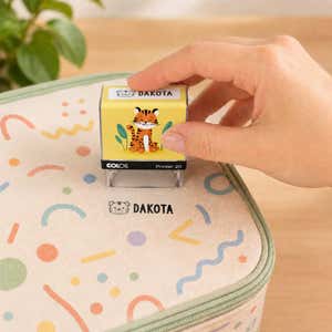 Hand using a tiger clothing name stamp to label a patterned lunch bag Dakota