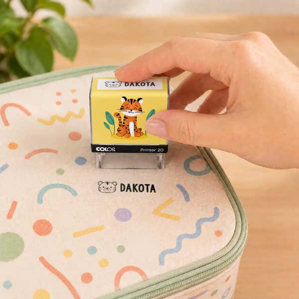 Hand using a tiger clothing name stamp to label a patterned lunch bag Dakota