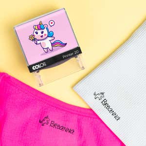 Pink unicorn clothing stamp beside pink and white shirts labeled Breanna