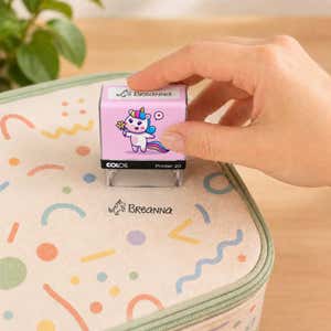 Hand using a unicorn clothing name stamp to label a patterned lunch bag Breanna