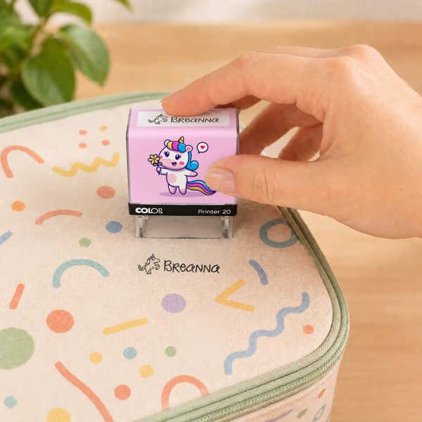 Hand using a unicorn clothing name stamp to label a patterned lunch bag Breanna