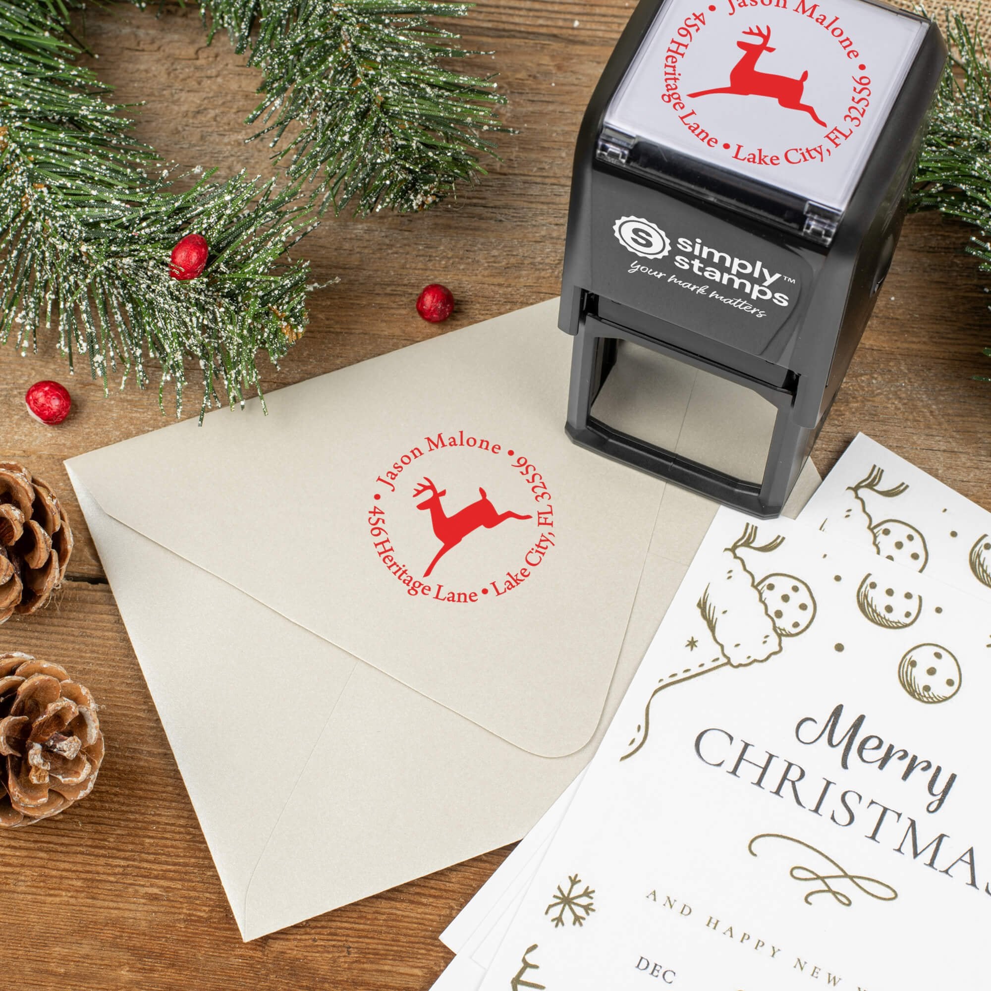 Holiday-themed ‘Leaping Reindeer Holiday’ address stamp shown on envelopes beside festive stationery, pinecones, and decorations.