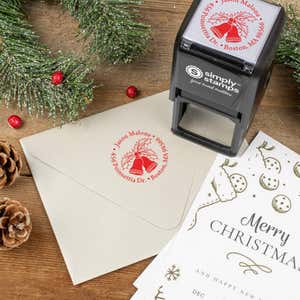 Holiday-themed ‘Holly Bells Holiday’ address stamp shown on envelopes beside festive stationery, pinecones, and decorations.