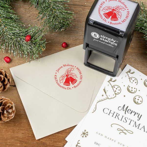 Holiday-themed ‘Holly Bells Holiday’ address stamp shown on envelopes beside festive stationery, pinecones, and decorations.