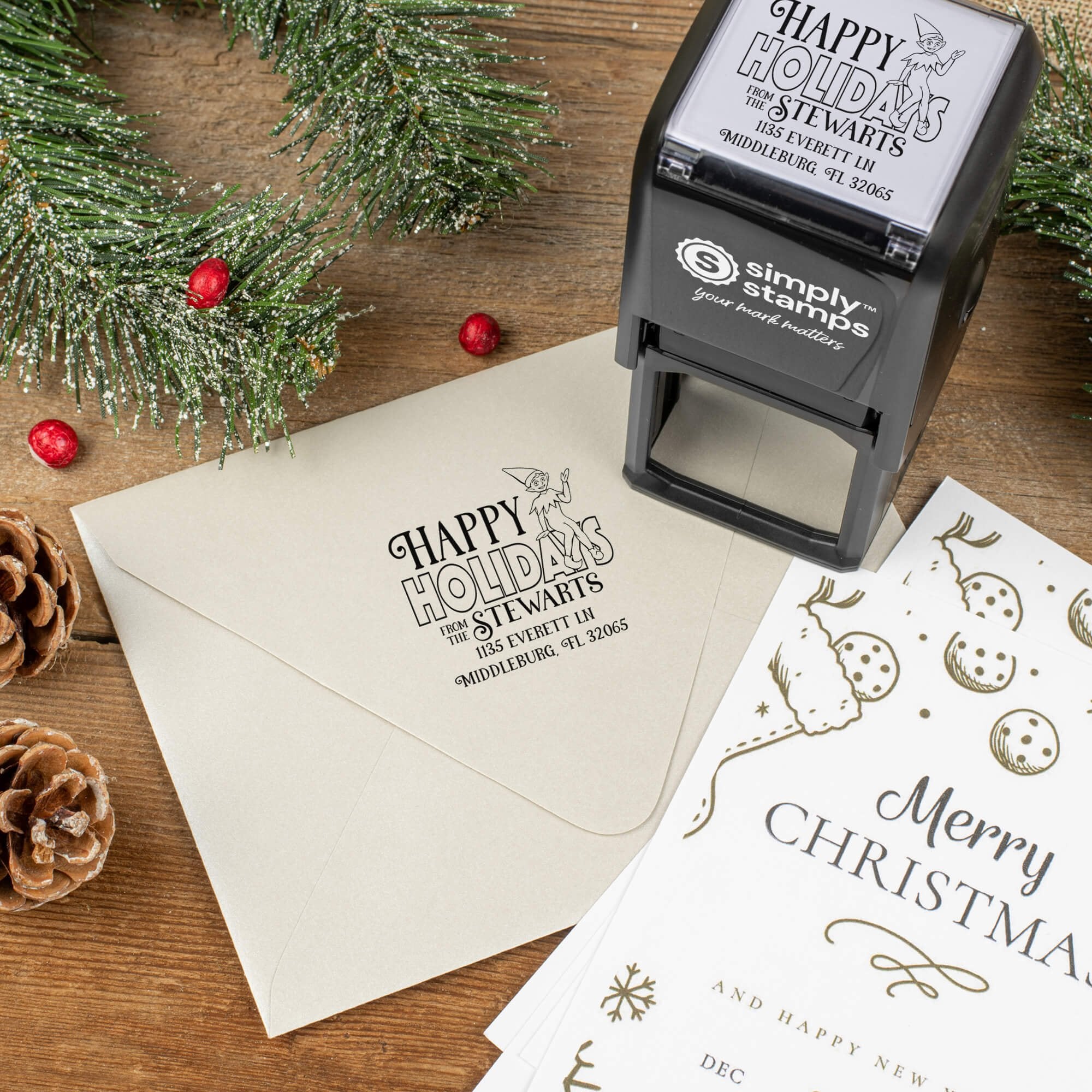Holiday-themed ‘Cartoon Elf’ address stamp shown on envelopes beside festive stationery, pinecones, and decorations.