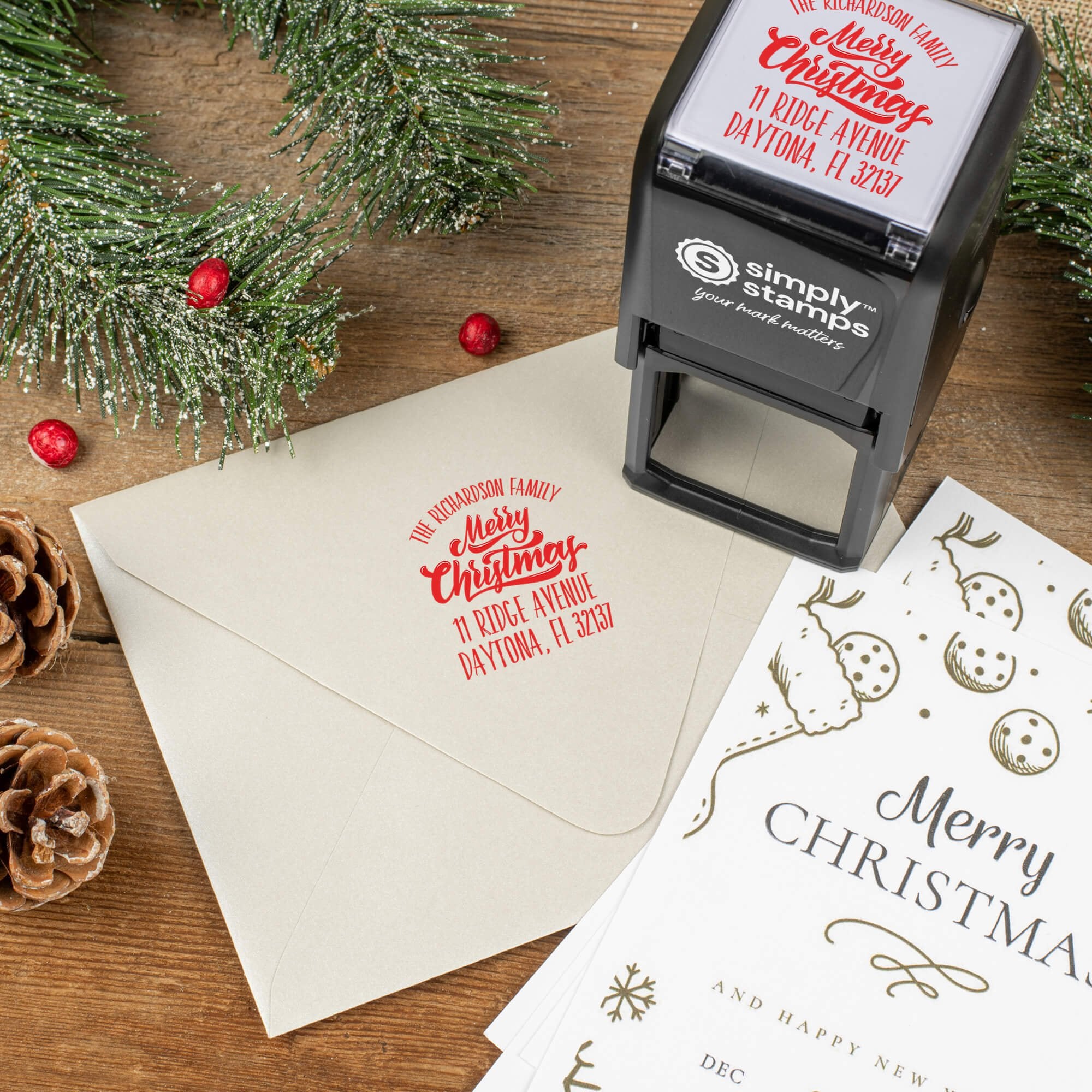 Holiday-themed ‘Classic Merry Christmas’ address stamp shown on envelopes beside festive stationery, pinecones, and decorations.