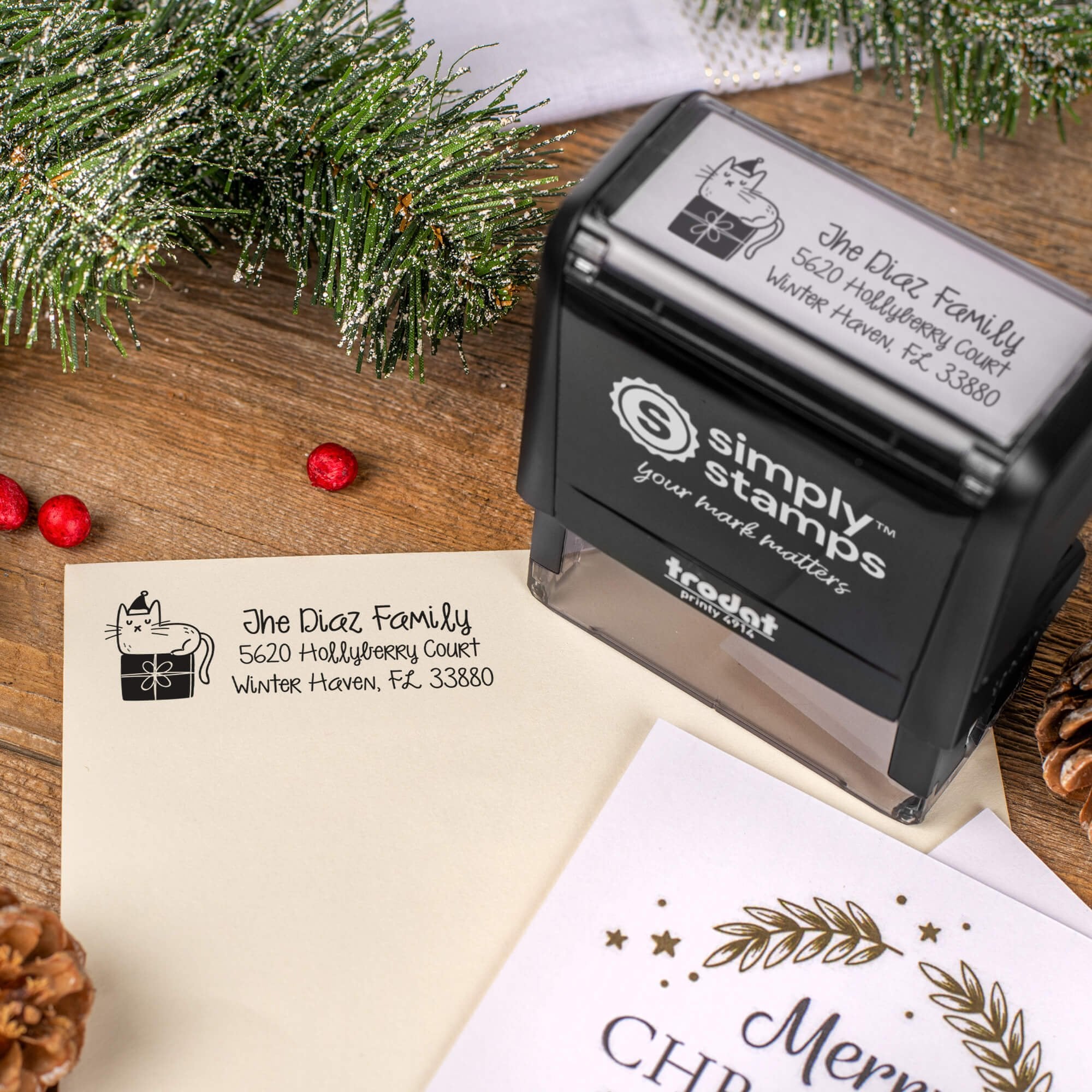 Holiday-themed ‘Holiday Cat’ address stamp, hand using self-inking Christmas tree address stamp to personalize a holiday envelope on festive wooden table.