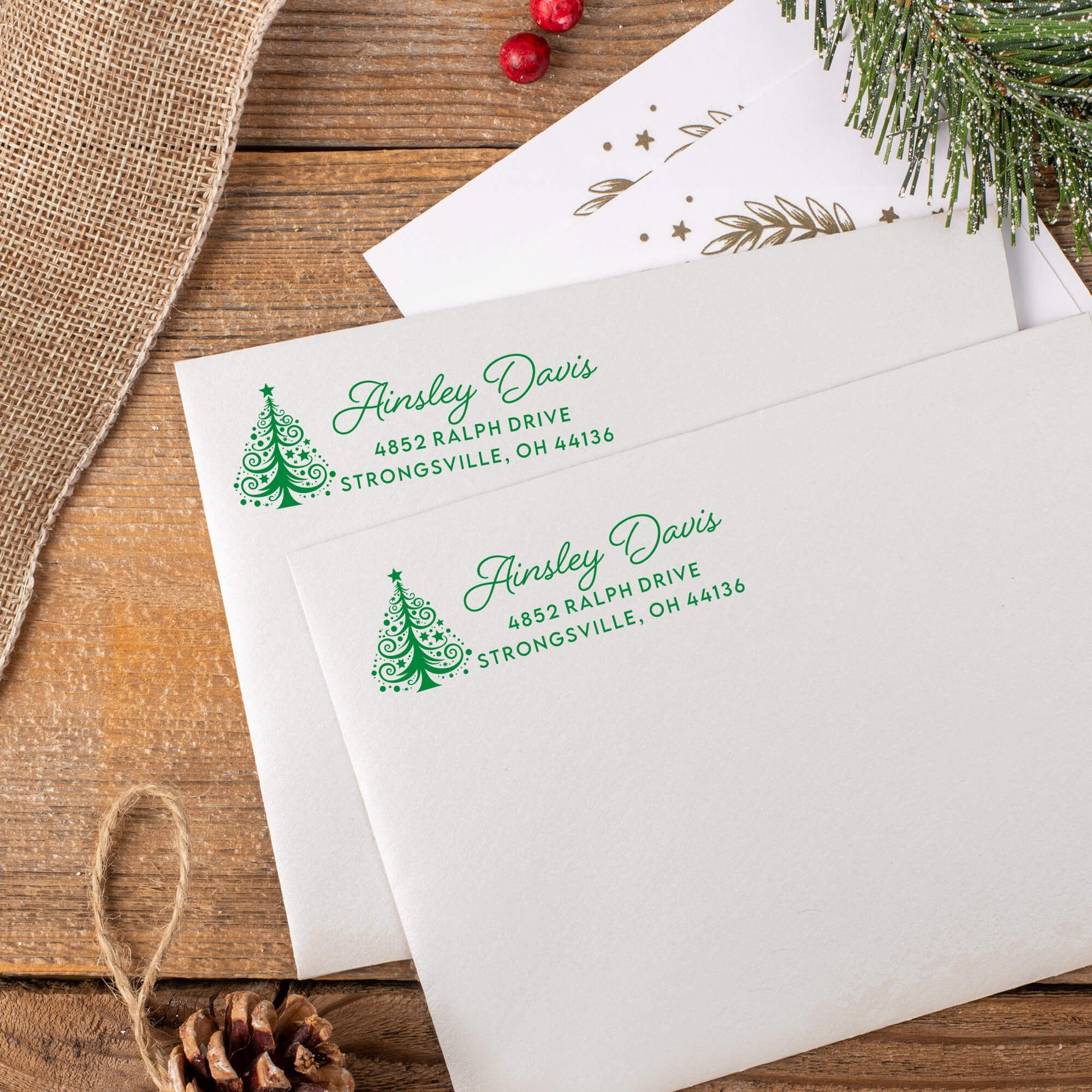 “Holiday return address stamp with a green swirled Christmas tree and custom name and address printed on white envelopes