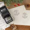 Holiday-themed ‘Magnolia Merry Christmas’ address stamp shown on envelopes beside festive stationery, pinecones, and decorations.