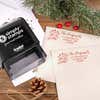 Holiday-themed ‘Let It Snow Winter Snowman’ address stamp, hand using self-inking Christmas tree address stamp to personalize a holiday envelope on festive wooden table.