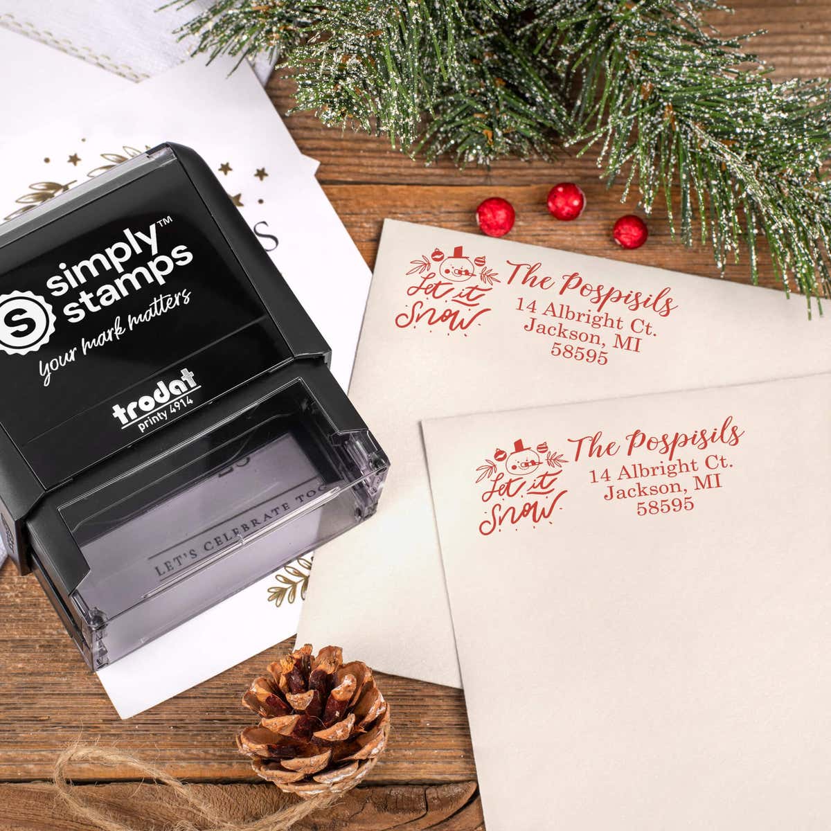 Holiday-themed ‘Let It Snow Winter Snowman’ address stamp, hand using self-inking Christmas tree address stamp to personalize a holiday envelope on festive wooden table.