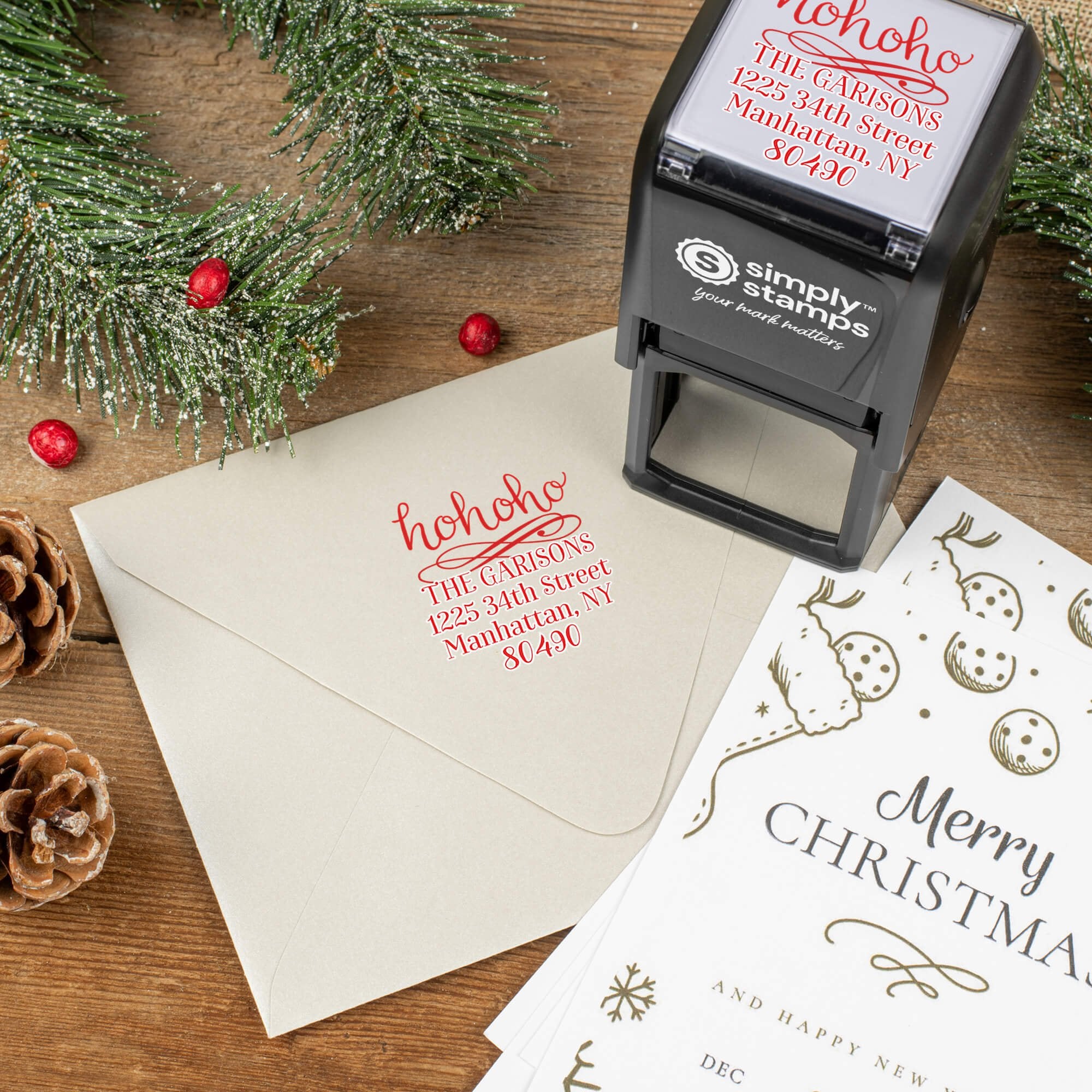 Holiday-themed ‘HoHoHo Christmas’ address stamp shown on envelopes beside festive stationery, pinecones, and decorations.