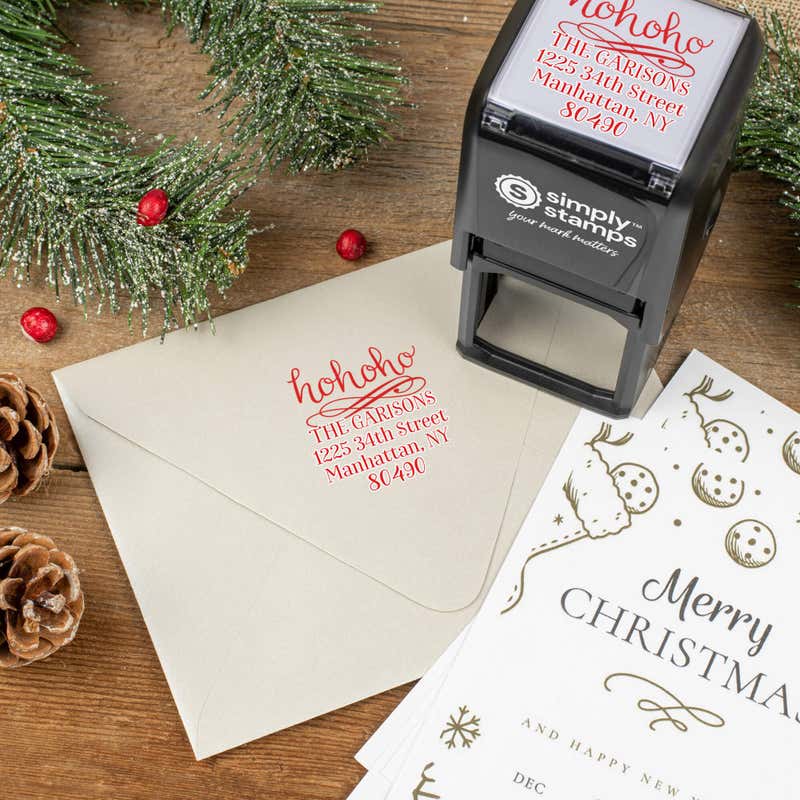 Holiday-themed ‘HoHoHo Christmas’ address stamp shown on envelopes beside festive stationery, pinecones, and decorations.