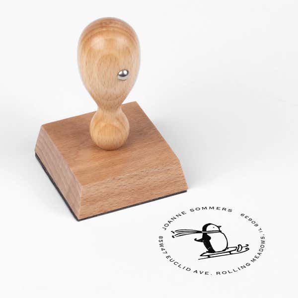European wood hand stamp shown from above featuring custom ‘Sledding Penguin Holiday’ holiday return address design.