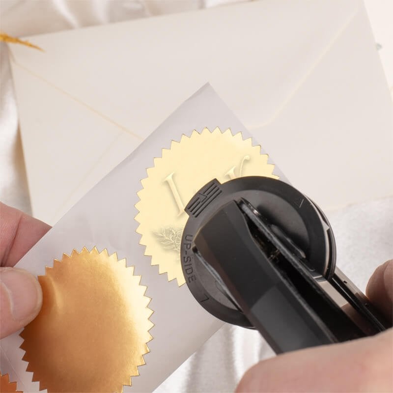 Hands using embosser tool to press personalized design into gold foil seals 