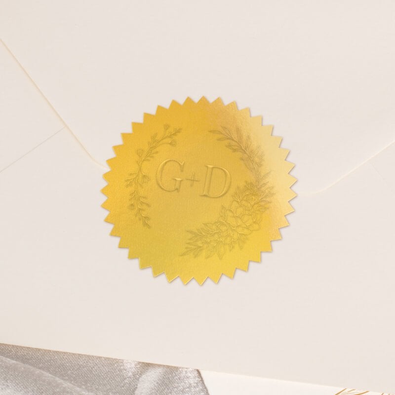 Round metallic gold seal embossed with custom wedding design on the back of an envelope