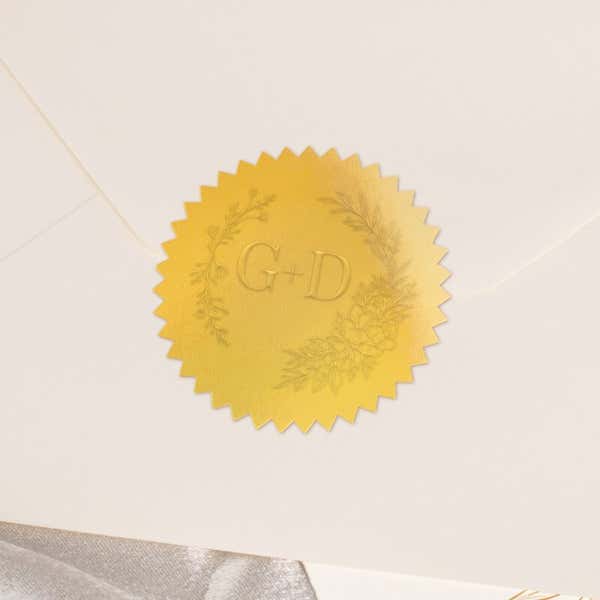 Round metallic gold seal embossed with custom wedding design on the back of an envelope