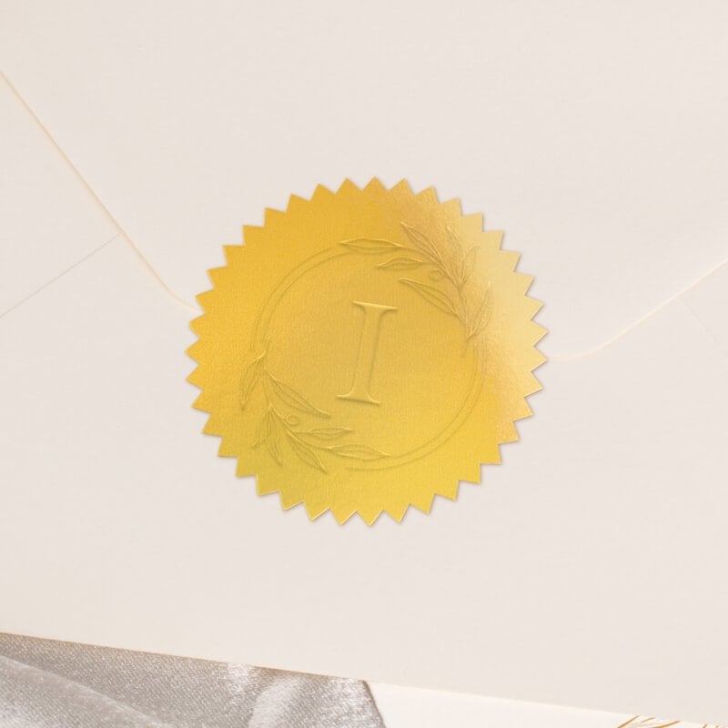 Round metallic gold seal embossed with custom wedding design on the back of an envelope