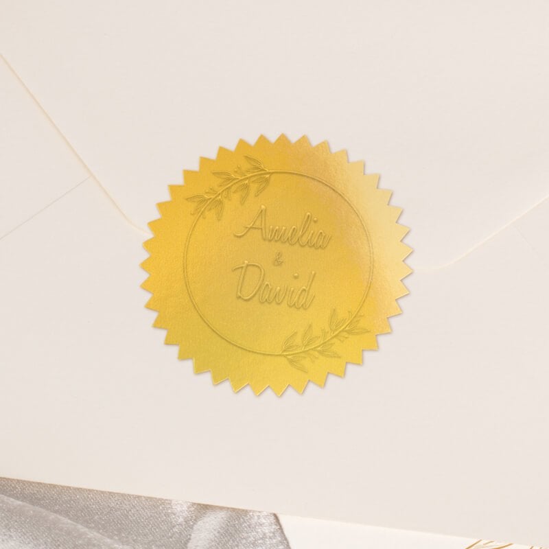 Round metallic gold seal embossed with custom wedding design on the back of an envelope