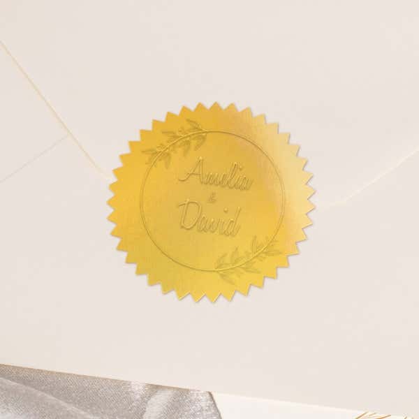 Round metallic gold seal embossed with custom wedding design on the back of an envelope