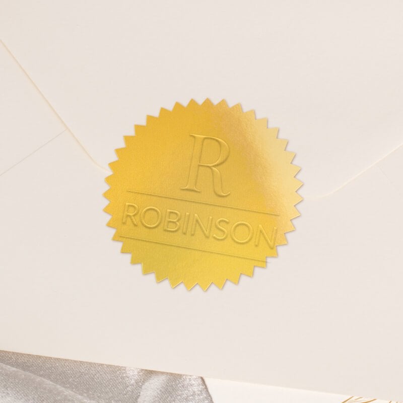Round metallic gold seal embossed with custom wedding design on the back of an envelope
