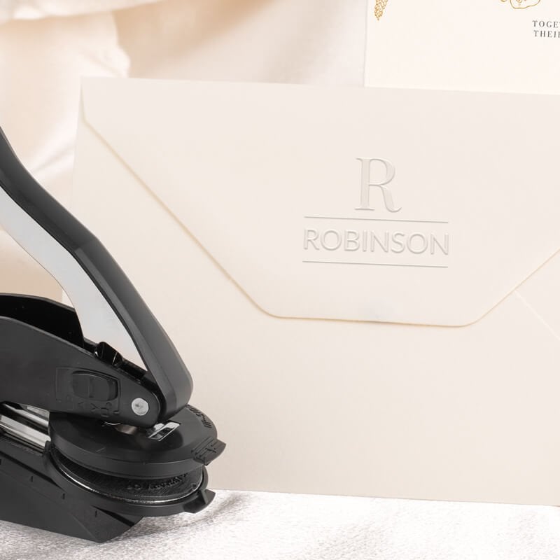 Embosser tool shown next to envelope that has been stamped with a custom wedding impression