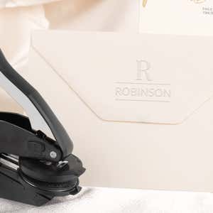Embosser tool shown next to envelope that has been stamped with a custom wedding impression