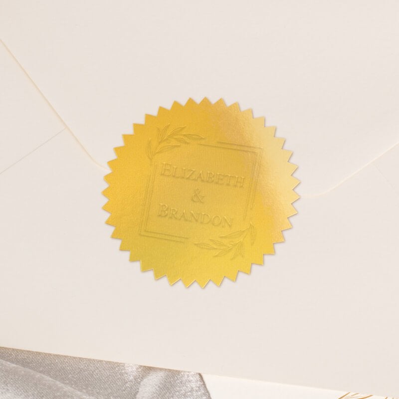 Round metallic gold seal embossed with custom wedding design on the back of an envelope