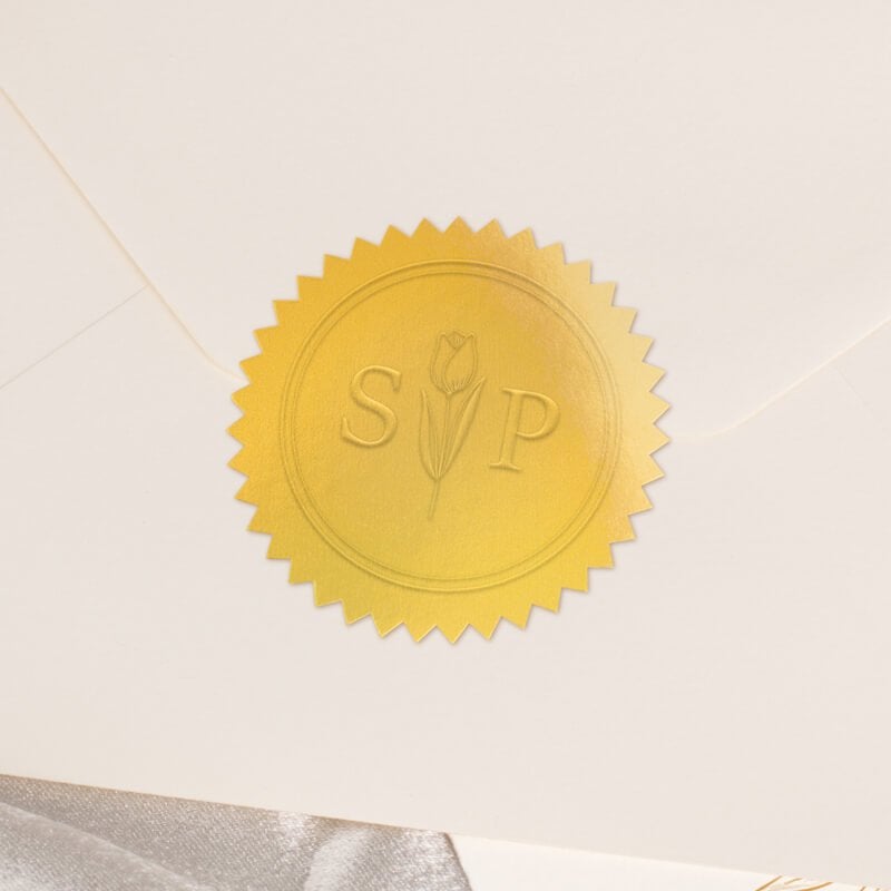 Round metallic gold seal embossed with custom wedding design on the back of an envelope
